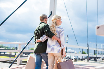 rear view of casual couple holding shopping bags while walking together on the bridge