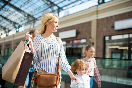 Mother With Shopping Bag In Hand Walking In Shopping Mall Together With Kids