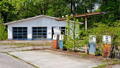 Vintage abandoned weed strew gas station: garage bays and pumps. Pre-convenience store era.