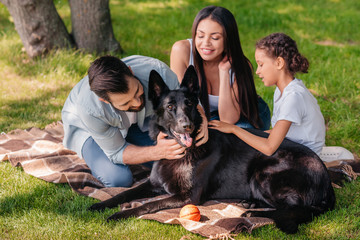 portrait of smiling family resting on blanket together with dog outdoors