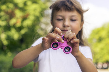 Little beautiful girl in white t-shirt is playing pink spinner in hand on the street