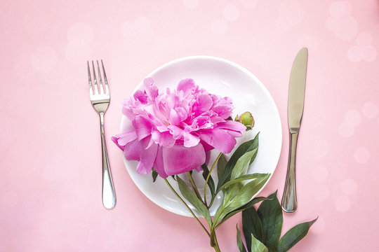 Festive table setting with cutlery and blooming peony on pink table.