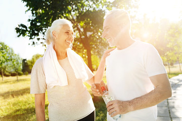 Positive aged couple resting in the park after sport activities