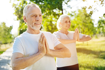 Positive sporty aged couple meditating in the park