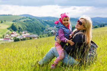 Happy mother with a child sitting on the grass on a background of forested mountains