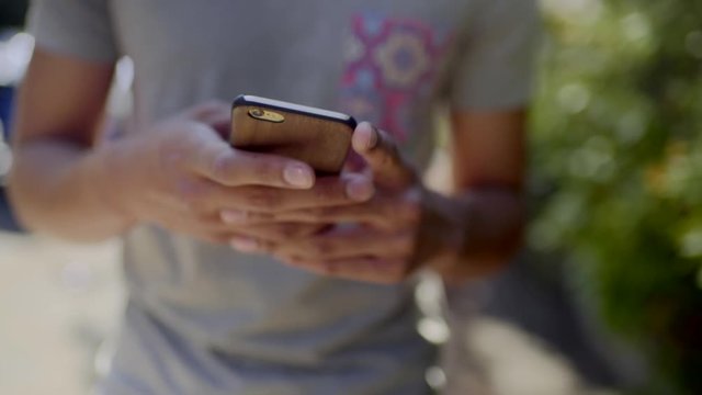 Closeup Of Young Man's Hands Using A Smart Phone As He Walks Through Neighborhood