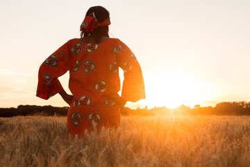 African woman in traditional clothes walking in a field of crops at sunset or sunrise