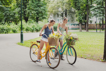 Happy boho chic girls gather wild flowers on bicycle ride