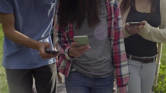 Group Of Friends Walk On Nature Trail, They Look At Their Phones, Show Each Other Texts, And Photos