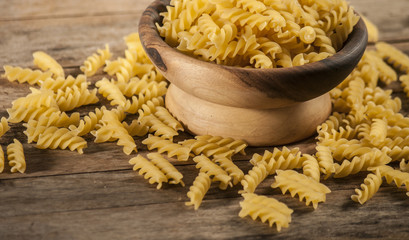 Pasta fusilli in a wooden bowl on wood background for healthy recipes.