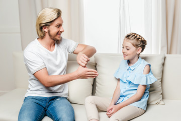 smiling father showing trick with finger to his daughter at home