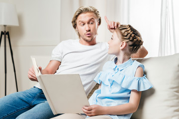 Obraz premium father pointing up while his daughter reading book and sitting on sofa at home
