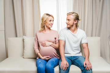 Happy pregnant couple sitting together on sofa and smiling each other