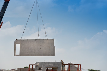 Construction site crane is lifting a precast concrete wall panel.