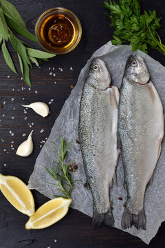 Two river trout on a board, with herbs, spices, lemon and pepper on wooden board, ready for cooking. Fresh fish