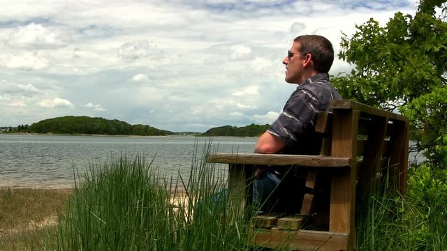 Man sits on beach bench enjoying midday sun overlooking Toby's island Pocasset Bourne Cape Cod