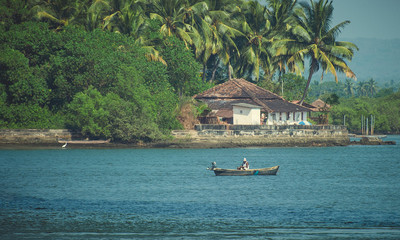 Fisherman in a boat on the river in the background house in palm trees