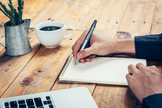 Hand business man writing notebook on wood table in coffee shop.