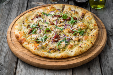 pizza with sun-dried tomatoes, prosciutto, arugula and parmesan cheese on a plate on the table