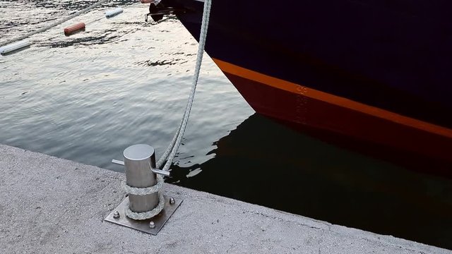 Leash sea knot pier bollard. Ship swinging on sea waves. Ship bottom in sea. Shine chrome bitt at pier. Sighn of strong friendship and affection concept.