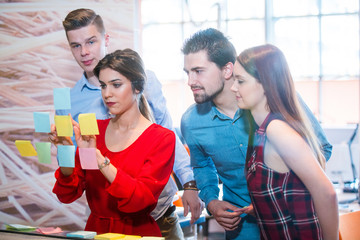 business, startup, planning, management and people concept - happy creative team with stickers on office glass board talking at office