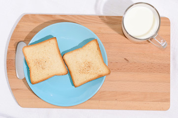 Square toast on a blue plate on a wooden board and a mug of milk