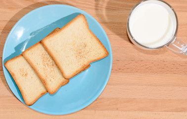 Square toast on a blue plate on a wooden board and a mug of milk