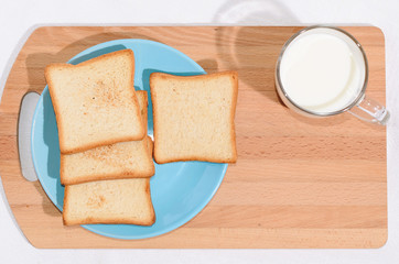 Square toast on a blue plate on a wooden board and a mug of milk