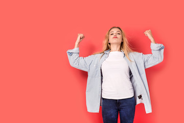 Young blonde girl shows her strength on red background - obrazy, fototapety, plakaty