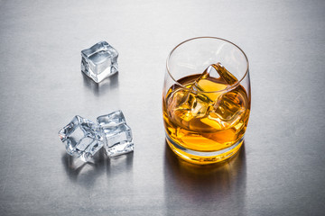Glass of whisky with ice on metallic background close up