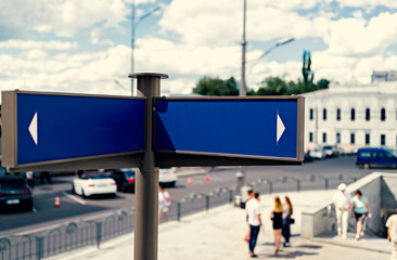 Blank blue street signs with city and people in blur on background, free space. Blank blue traffic road signs, free space for text. Blank street sign on cloudy sky background, copy space