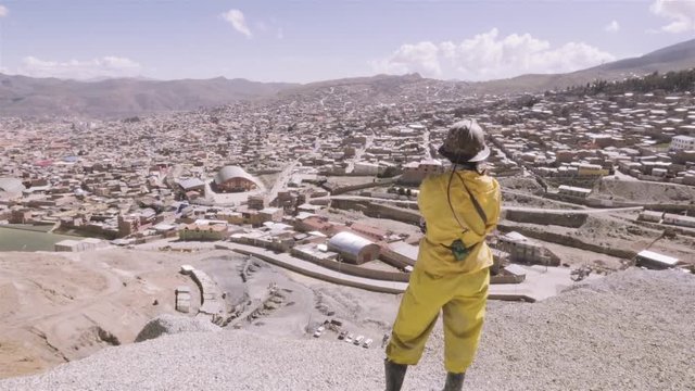 Miner wearing a yellow suit, helmet and boots contemplating the cityscape of Potosi before shitf on the mine