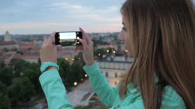 A sweet girl, a traveler on a viewing platform, takes pictures of the city.