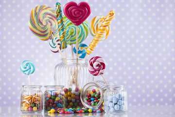 Candies in glass jars on color wooden background