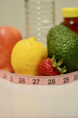 Water apple lemon strawberry avocado honey wrapped in a measuring tape representing waist line portraying the elements for good health and fitness shot from the front on a white background