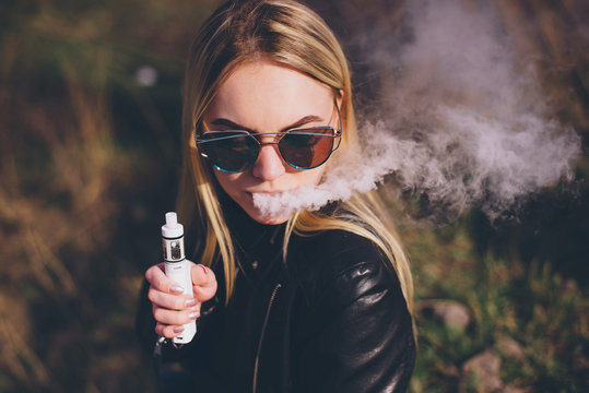 Happy vaper girl with vaping device in hand.Quit smoking nicotine cigarettes,start vaporizing.Tasty fruit flavor e-liquid or e-juice.Attractive young woman
