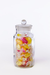 Confectionery. Jar of boiled sweets in wrappers isolated against white background. Yellow and pink candy.