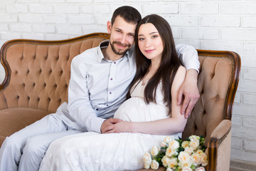 family and parenthood concept - young beautiful pregnant couple sitting on vintage sofa