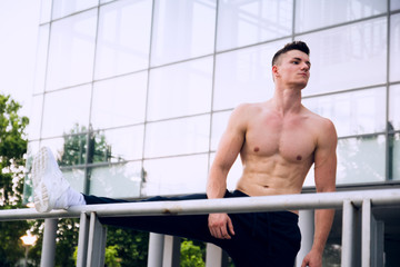 Young man stretching his leg after a heavy workout. Wearing tracksuits without shirt. Selective focus.