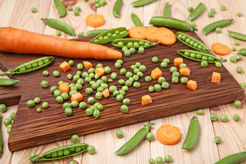 Green peas and carrots sliced on wooden table