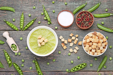 Green peas soup in bowl with salt and pepper on wooden table