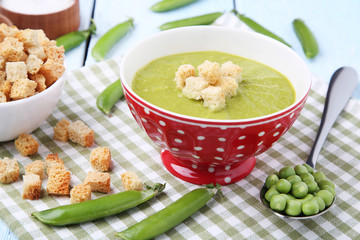 Green peas soup in bowl with rusks on wooden table