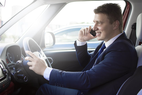 Businessman driving his car while talking on the phone. Smiling and talking while in traffic. Suit and tie businessman sitting in his automobile.