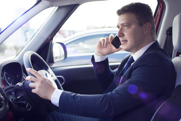 Businessman driving his car while talking on the phone. Smiling and talking while in traffic. Suit and tie businessman sitting in his automobile.
