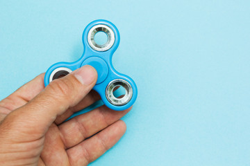 Male hand holding popular fidget spinner toy on the blue background