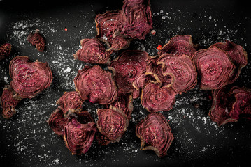 Organic diet food. The vegan diet. Dried vegetables. Homemade chips from beets. On black plate, top view