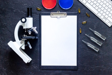 Workplace in laboratory. Microscope, syringe, Petri dish, pad and pills on grey stone background top view mockup