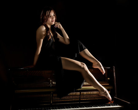 beautiful young woman in a black dress with an open back sitting on a old piano on a dark background