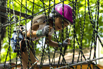Happy 5 year old girl in pink protective helmet and equipment in a rope park in summer.