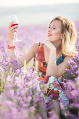 Beautiful blonde sexy woman is drinking red dry wine in lavender field